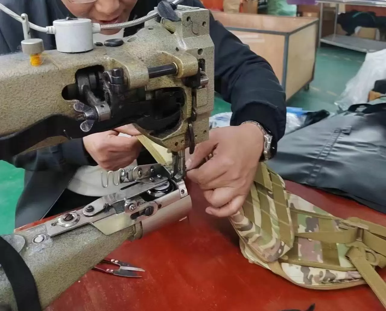 Technician operating a heavy-duty sewing machine to stitch camouflage fabric for tactical gear, showcasing precision craftsmanship and rugged material handling